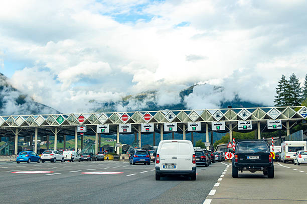 Vehicles line up at highway toll booths with mountains and low clouds visible in the background.