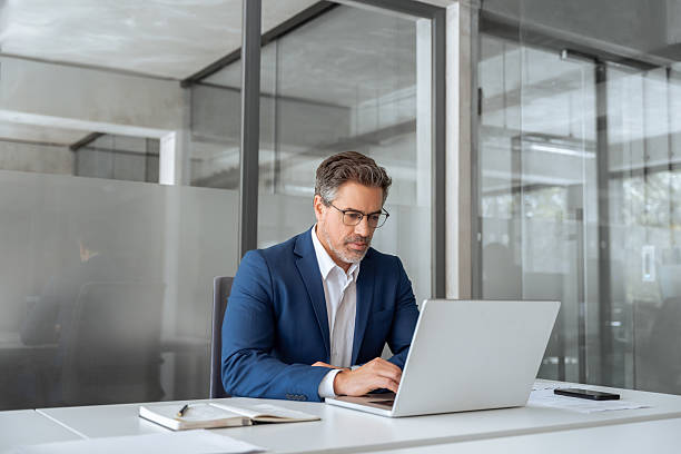 istock Mature indian ceo business man in suit using pc laptop for trading, looking focused at screen. Middle age latin male entrepreneur businessman working on financial work at desk in office. Copy space 2213729802