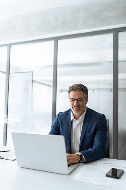 istock Busy latin male executive businessman looking on computer thinking, working on finance data sitting at desk in office. Mature indian business man in suit using pc laptop for trading work. Vertical 2213729803