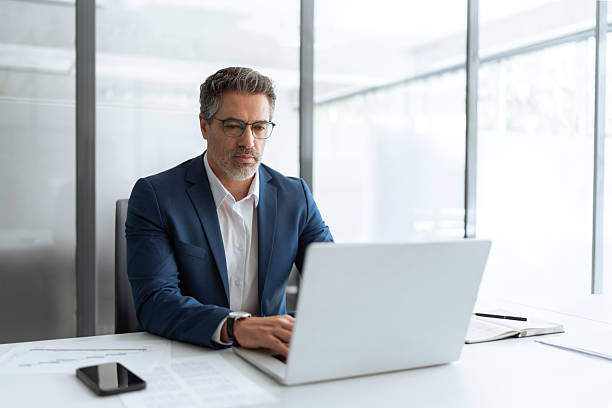 istock Busy latin male executive businessman looking on computer thinking, working on finance data sitting at desk in office. Mature indian business man in eyeglasses, suit using pc laptop for trading work 2213729825