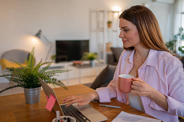 istock Young woman working from home drinking coffee and using laptop 2213730875