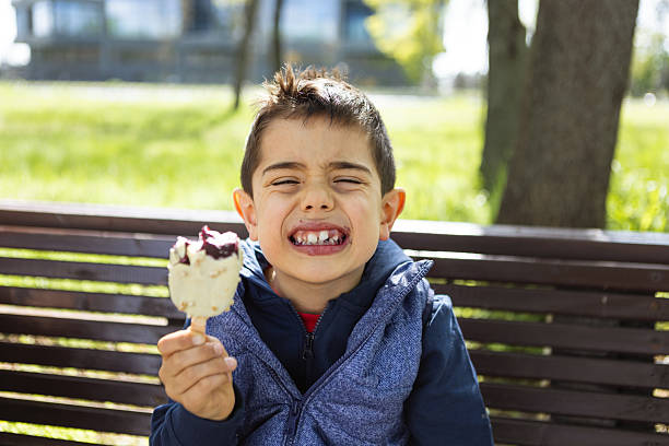 Happy little boy enthusiastically eating tasty ice cream outdoors in summer. School child have snack on the go after school on sunny day. The kid eats delicious ice cream and gets dirty.