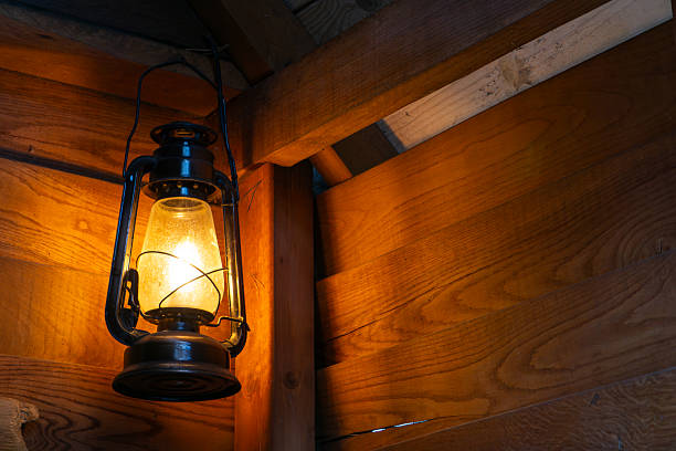 istock glowing kerosene lantern hanging inside a wooden structure, casting warm light on natural wood planks. The scene captures a cozy, vintage atmosphere, perfect for illustrating rustic interiors, cabin life, or nostalgic lighting in traditional settings. 2213733175