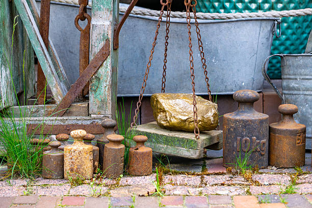 collection of old cast iron weights arranged beside a weathered platform scale, set against a rustic background with a metal tub and wooden frame. The scene evokes a retro, industrial atmosphere, capturing the essence of historical craftsmanship and rural life