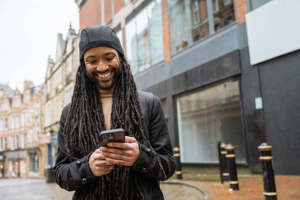 istock Black tourist with dreadlocks visiting city on rainy day and using smart phone for text messaging 2213735952