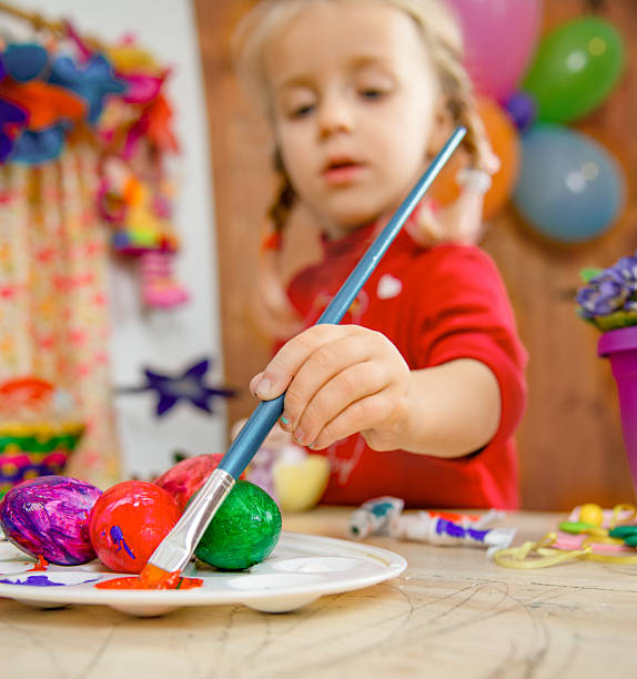 Little girl painting colorful Easter eggs during a fun art and craft activity. Close-up on the hand with paintbrush. Concept of creativity, childhood, and holiday celebration.