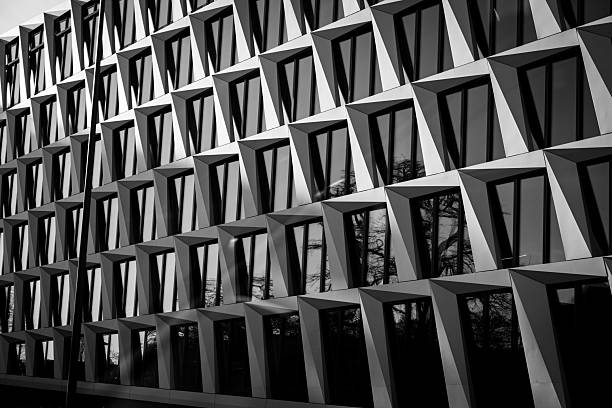 Black and white geometric facade of a modern building with reflective windows creating an abstract pattern.