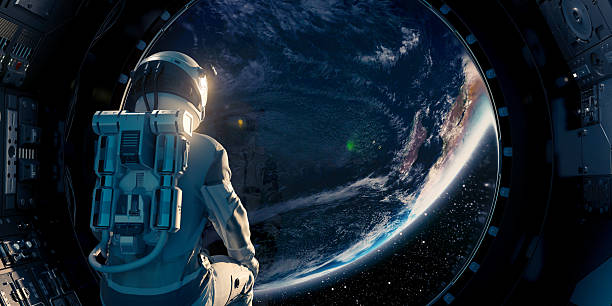 A single astronaut from behind sitting on a spacecraft or space station surrounded by control panels looks thorugh a porthole window towards a planet Earth.