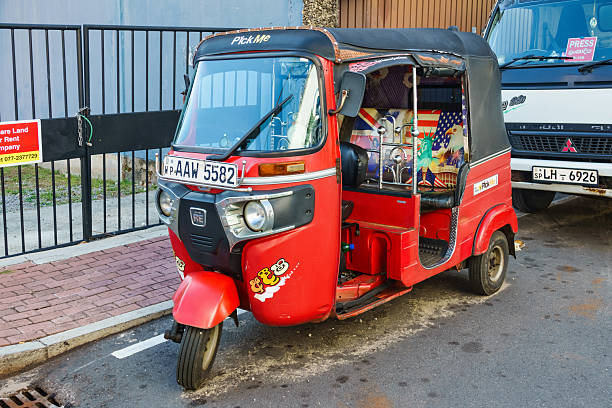 A red colored tuk-tuk is parked on a street in Colombo, Sri Lanka on cloudy day.