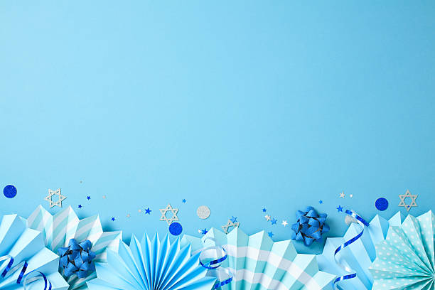 istock Blue Hanukkah decorations on a light blue background, featuring paper fans, gift bows, Star of David cutouts, and glitter accents. 2213744149