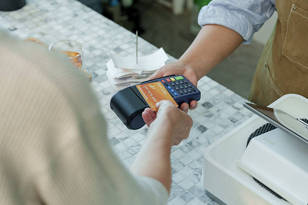 istock Customer tapping orange credit card on payment terminal at cafe counter demonstrating contactless payment and cashless transaction in modern small coffee shop 2213744332