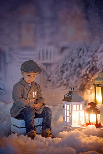 istock Little boy, looking at flame from match, sitting in the snow 2213744587