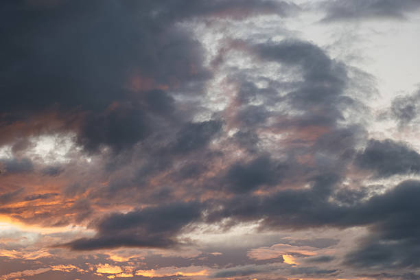 Dramatic sky with gray clouds and hints of orange light during sunset over a peaceful landscape