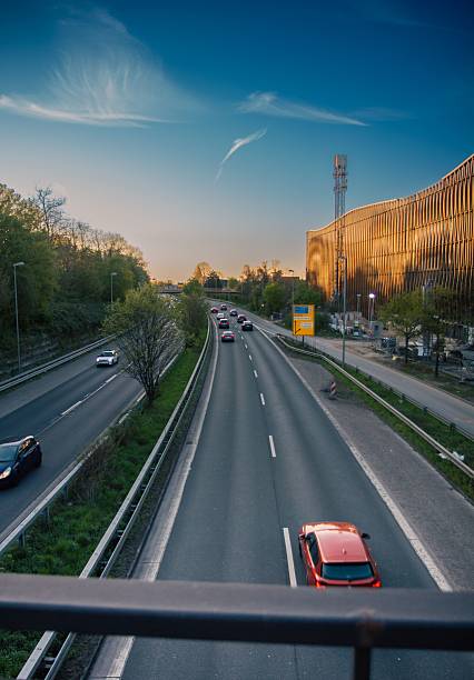 A highway scene with cars under a blue sky, featuring modern architecture in the background during sunset.