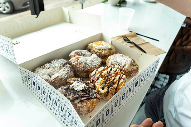 istock A person is currently holding a large box filled with donuts on a table 2213751079