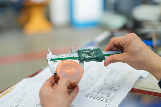 Close-up of a technician measuring a part with a caliper, with the part and technical drawing visible