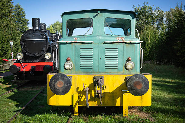 A green train with yellow trim sits next to a black train. The green train is old and rusty