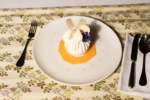 Elegant Plated Dessert with White Chocolate and Edible Flowers Elegant plated dessert featuring a layered pastry topped with whipped cream, thin white fruit slices, and a delicate purple flower, placed on an octagonal orange base with syrup accents. plated chocolate dessert stock pictures, royalty-free photos & images