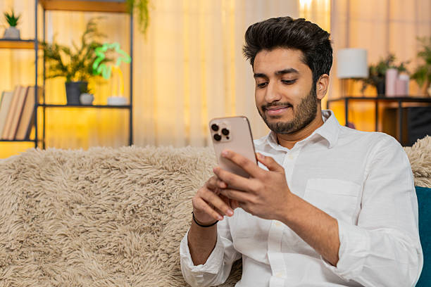 istock Indian man sits on sofa focused on smartphone typing text reading news responding to messages work 2213759968