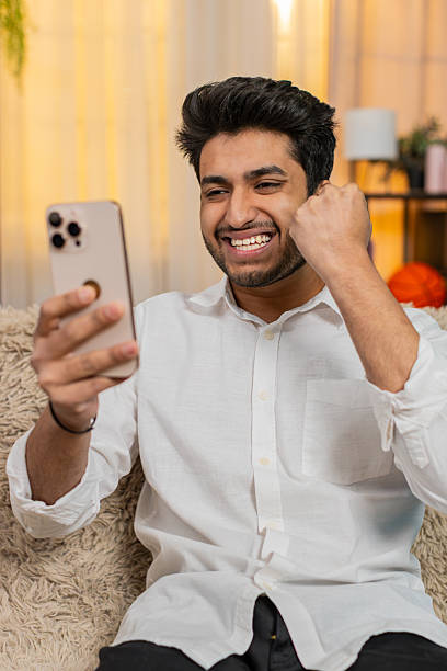 istock Indian joyful man on sofa happily texting on smartphone, celebrating lottery win, joyful expression 2213759970