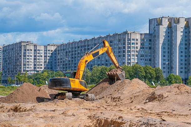 istock A large excavator is at work, digging into a mound of soil at a construction site. Tall residential buildings stand in the background under a clear sky 2213760685