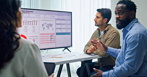 istock Group of business professionals meeting reviewing global data analytics presented on a large screen, discussing strategy and growth at the office. Finance meeting concept. 2213765677