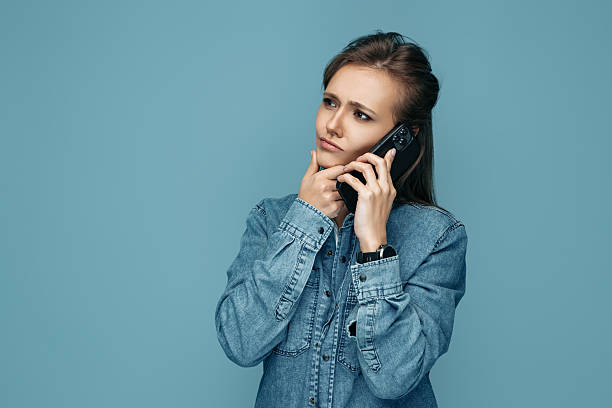 istock Thinking young woman talking on smartphone over blue background. 2213771217