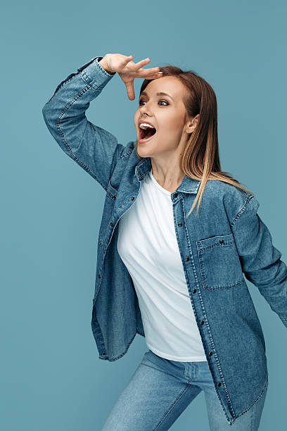 Joyful young woman in jeans shirt wearing headphones looking away with hand over eyes Joyful young woman in jeans shirt wearing headphones looking away with hand over eyes. hair covering eyes stock pictures, royalty-free photos & images
