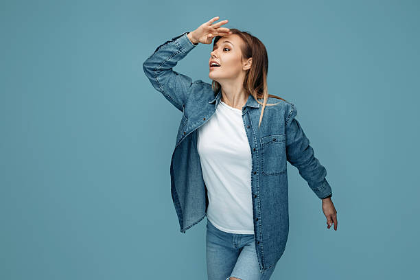 Curious woman in jeans shirt wearing headphones looking away with hand over eyes Curious woman in jeans shirt wearing headphones looking away with hand over eyes. hair covering eyes stock pictures, royalty-free photos & images