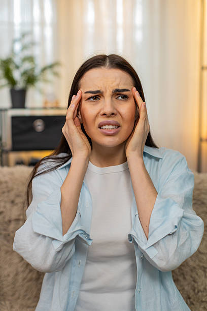 istock Young woman sitting on sofa holding head suffering from strong headache feeling uncomfortable pain 2213772665