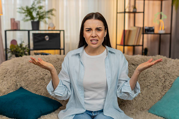 istock Young woman sitting on sofa making what face expression looking confused shocked surprised reaction 2213772676