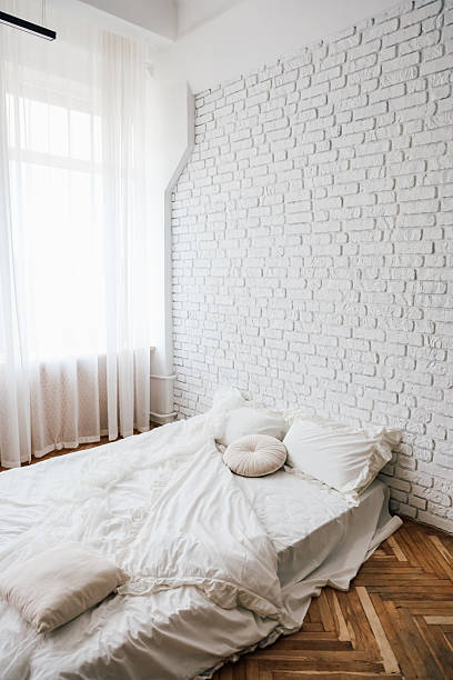 istock Cozy minimalist bedroom with white brick wall and soft bedding in natural light 2213773531