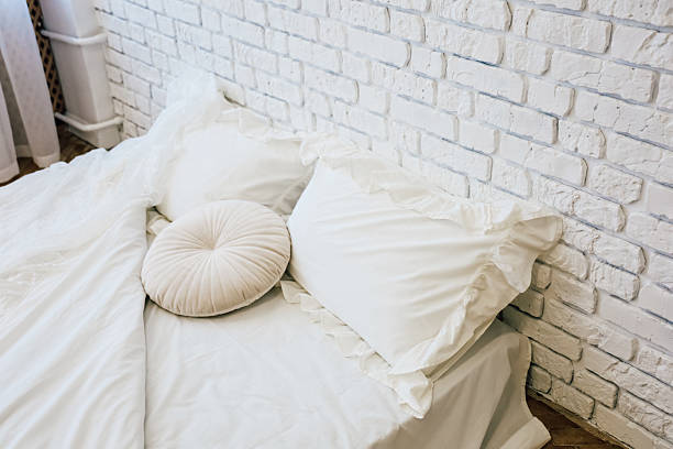 Cozy bedroom with white bedding and decorative pillow on a brick wall backdrop