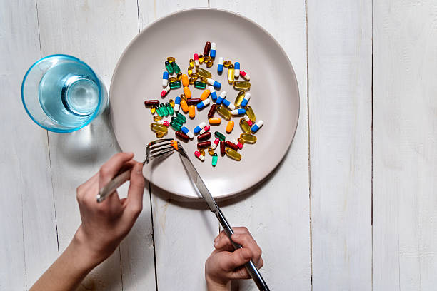 istock Pills and supplements served as meal concept. Assorted colorful capsules and tablets on a plate being eaten with fork and knife, representing pharmaceutical dependency or modern nutrition. 2213776956
