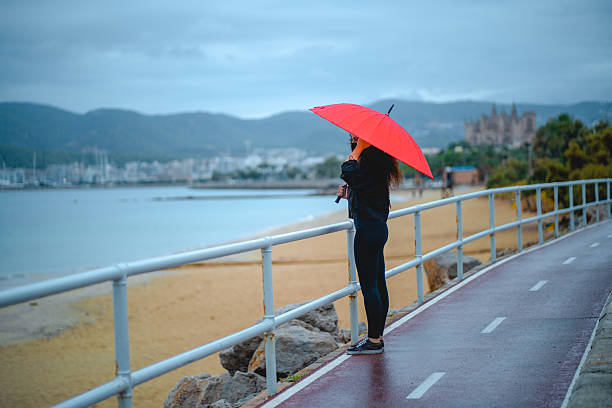 istock Woman with red umbrella enjoying coastal view 2213776961