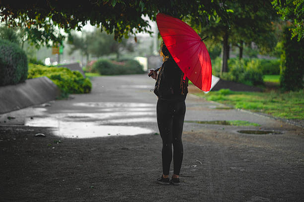 istock Woman standing with red umbrella in rainy park path 2213778023