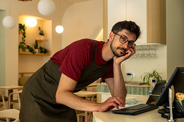 istock Young waiter leaning on the counter looking at camera 2213778876