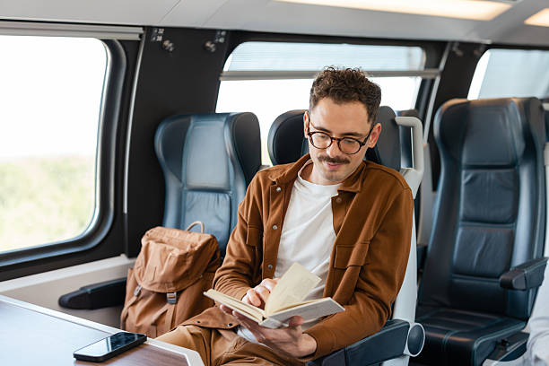 istock Man reading a book while traveling in a modern train 2213782248