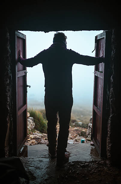 Man standing in a doorway, gazing out at a fog-covered landscape, with open doors framing his silhouette in a scene filled with mystery and adventure