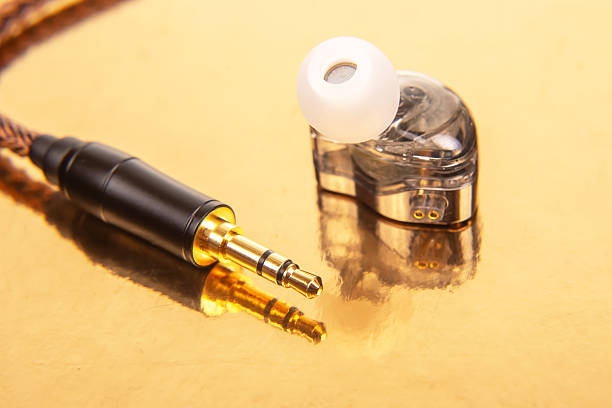 A single earbud with a white tip, a 3.5mm audio jack, and a black audio device on a reflective gold surface. Ideal for tech and audio themes.