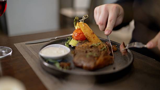 istock A man cuts a cooked steak from medium-sized ribs. Delicious steak with vegetables on the table. A man in a restaurant eats, cuts meat with a knife. 2213796142