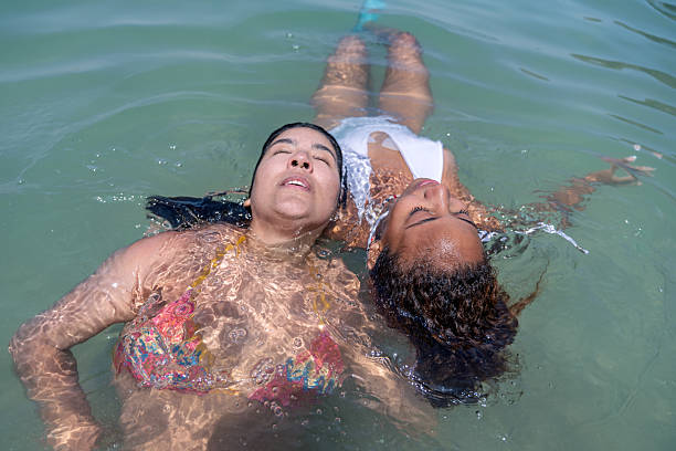 Two multiracial female friends are floating in the ocean, enjoying a relaxing day at the beach