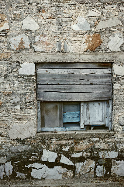 A timeworn stone facade featuring a window covered by aged wooden planks. The textures evoke history and resilience, a perfect symbol of rustic charm and forgotten eras.