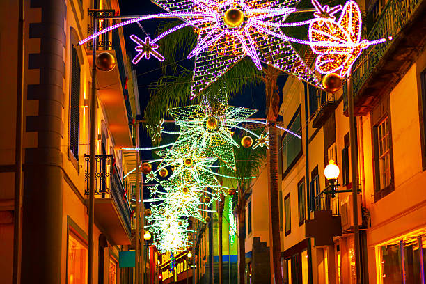 Festive street scene, adorned with vibrant Christmas lights in Funchal Madeira. Warm illumination reflects off the facades, creating a magical holiday atmosphere under the night sky