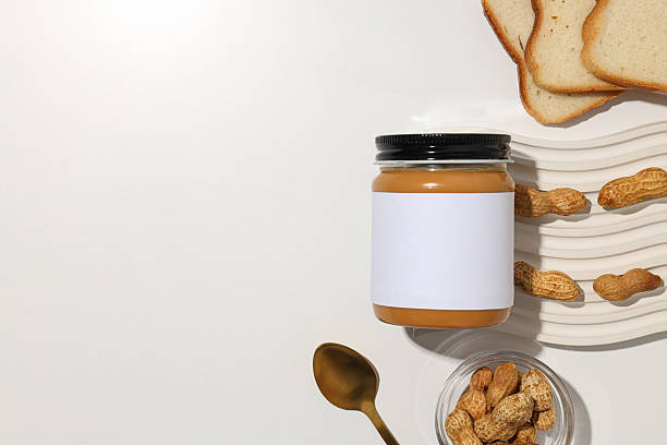 Peanut paste in a glass jar with a spoon, on a light background.
