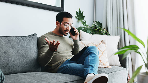 istock Phone call, frustrated and man on sofa in home for communication, social networking and chatting. Living room, crisis and person on smartphone for talking, online contact and conversation for issue 2213829320