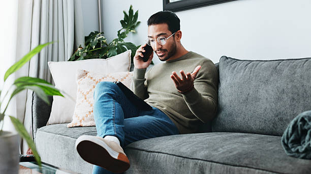 istock Phone call, stress and man on sofa talking in home for communication, network issue and conflict. Living room, house and frustrated person on smartphone for crisis, online conversation and connection 2213829322