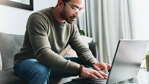 istock Glasses, online and laptop with man on sofa for freelancer, networking or email response. Reading, communication and remote worker with person in living room of home for business proposal or research 2213829386