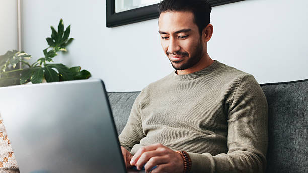istock Research, online and laptop with man on sofa for freelancer, networking and email response. Reading, communication and remote worker with person in living room of home for business proposal or typing 2213829388