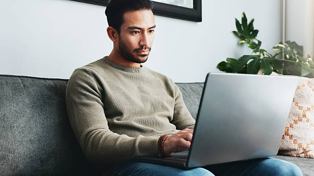 istock Typing, relax and laptop with man on sofa for freelancer, networking and email response. Reading, communication and remote worker with person in living room of home for business proposal or research 2213829389
